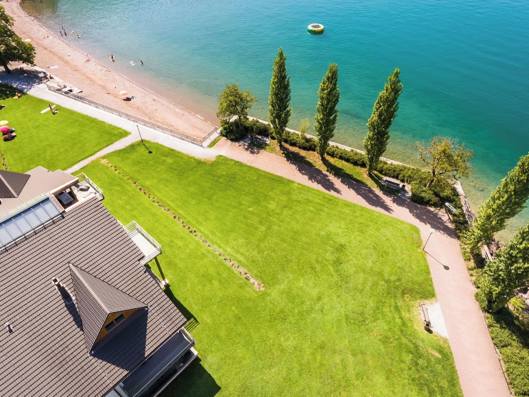 Un quartier résidentiel avec une pelouse bien entretenue, un sentier et une plage où l’on peut voir des gens et une plateforme flottante.