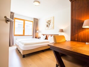 A hotel room with a bed, a desk, and a window with curtains.