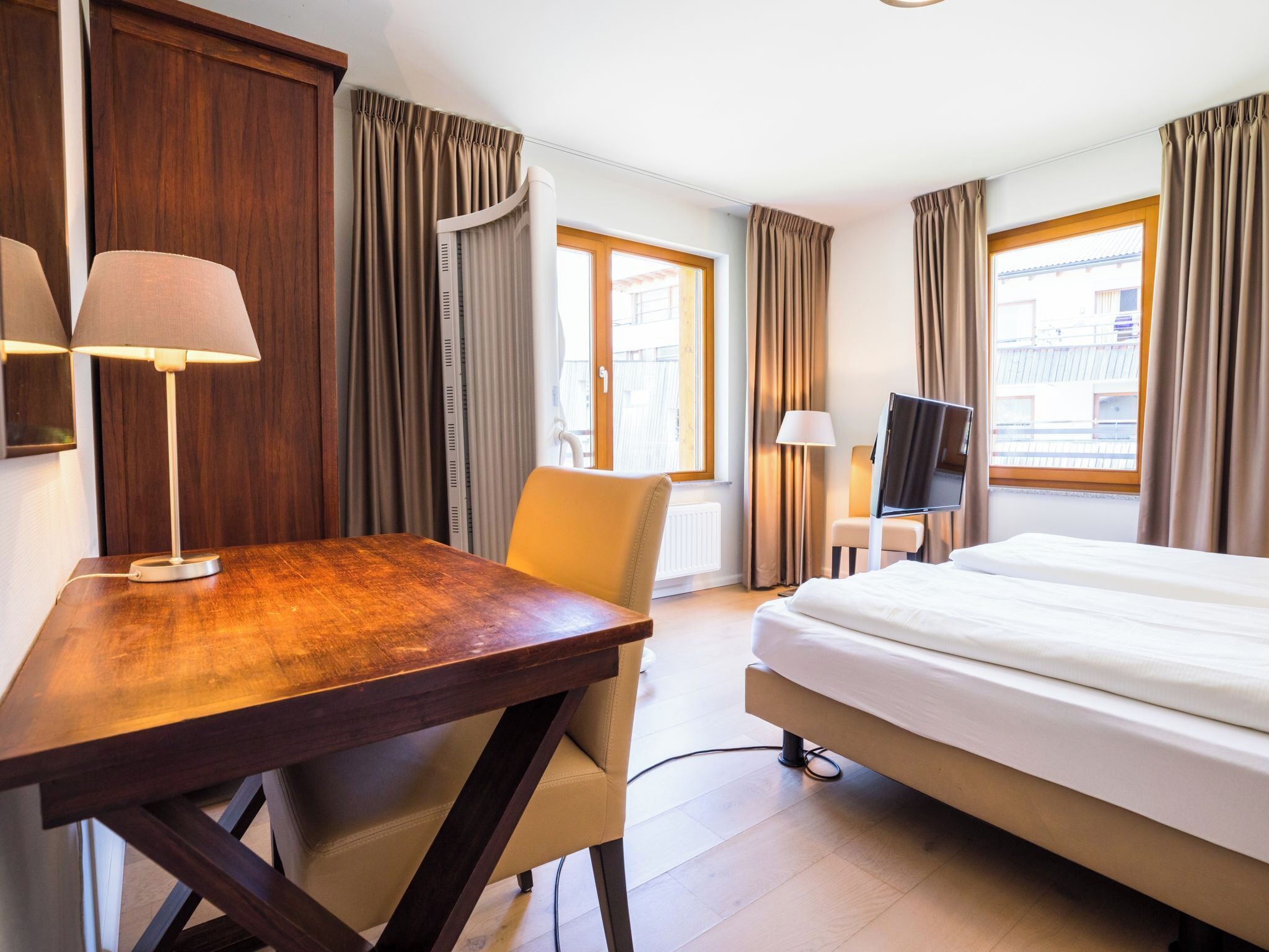Une chambre d’hôtel avec un lit, un bureau, une chaise, une télévision et des rideaux.