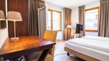 Une chambre d’hôtel avec un lit, un bureau, une chaise, une télévision et des rideaux.