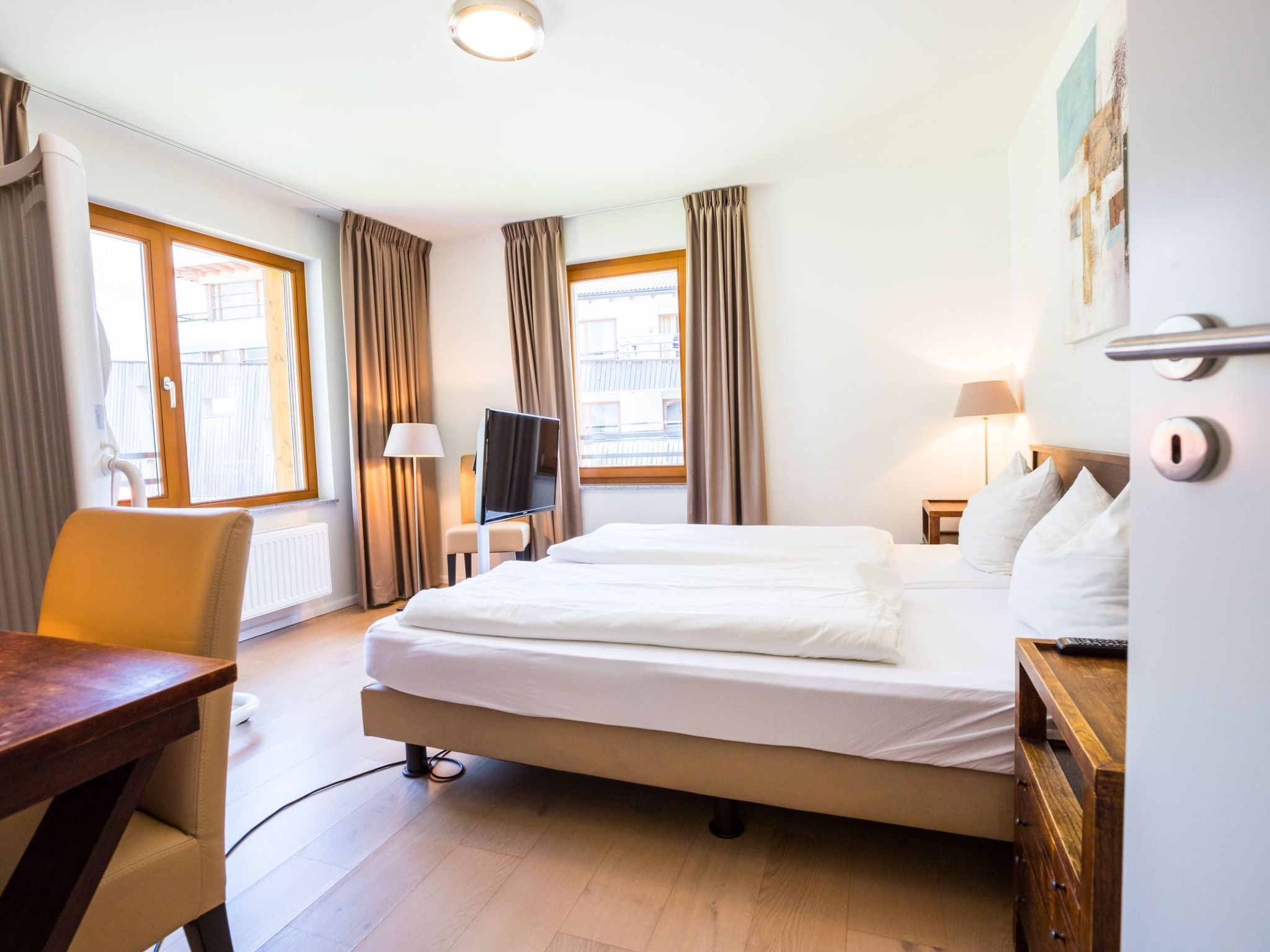 A hotel room with a bed, a desk, a chair, a TV, and a window with curtains.
