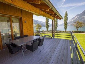 A wooden deck with a table and chairs, overlooking a lake and mountains.