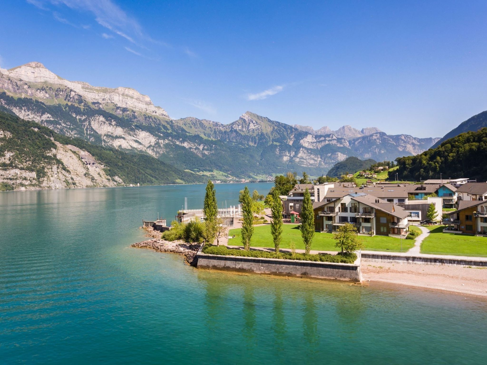 Un hotel frente al lago con vista a las montañas, un muelle y un césped bien cuidado.
