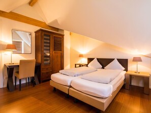 Un dormitorio con cama doble, un armario de madera, un escritorio con silla y dos lámparas de noche.