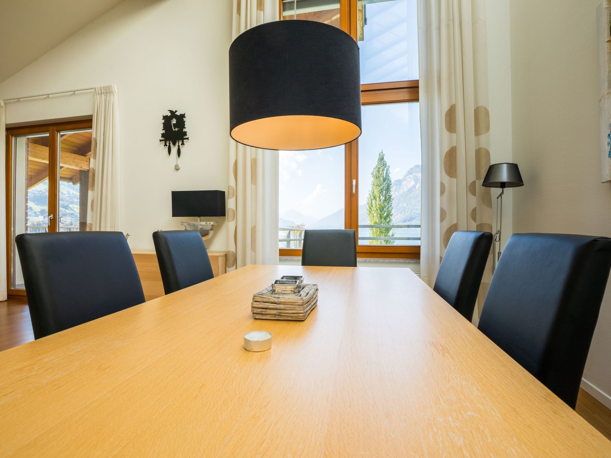 Une salle de conférence avec une table en bois, des chaises noires, une lampe et une vue sur les montagnes grâce à de grandes fenêtres.
