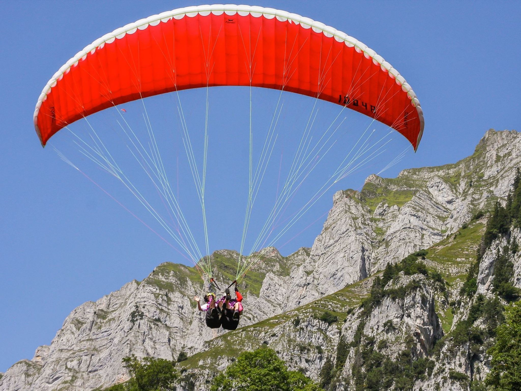 A person paragliding with a red canopy over a mountainous landscape.