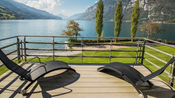 Varanda com duas cadeiras de descanso com vista para um lago e montanhas ao fundo.