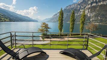 Un balcon avec deux fauteuils de jardin donnant sur un lac, avec des montagnes en arrière-plan.
