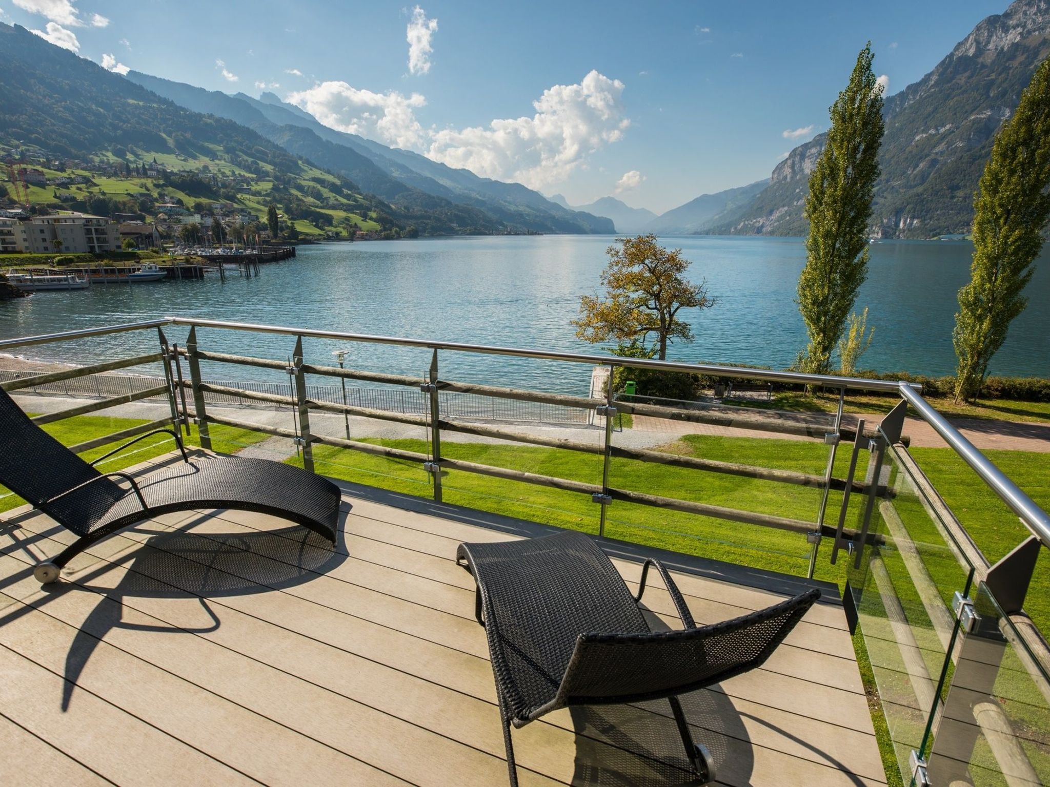 A deck with two lounge chairs overlooking a lake with mountains in the background.
