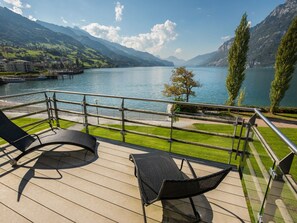 Eine Terrasse mit zwei Liegestühlen mit Blick auf einen See, im Hintergrund Berge.