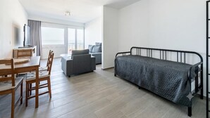 Moderni, hyvin valaistu huone, jossa on ruokapöytä, tuoleja, sohva, sänky ja televisio.