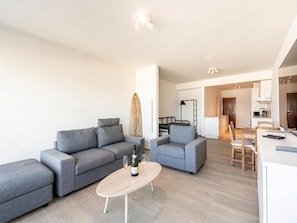 A modern living room with grey sofas, a wooden coffee table, and a surfboard on the wall. - Classy studio with sea view. (Blankenberge)