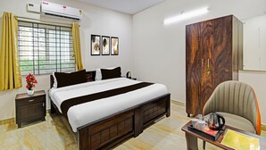 Une chambre d’hôtel comprenant un lit, une armoire, un bureau avec une bouilloire, une chaise et une fenêtre avec des rideaux.