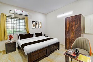 Een hotelkamer met een bed, een kledingkast, een bureau met waterkoker, een stoel en een raam met gordijnen.