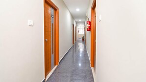 Un couloir avec des portes de chaque côté, un extincteur fixé au mur et une plante en pot au bout.