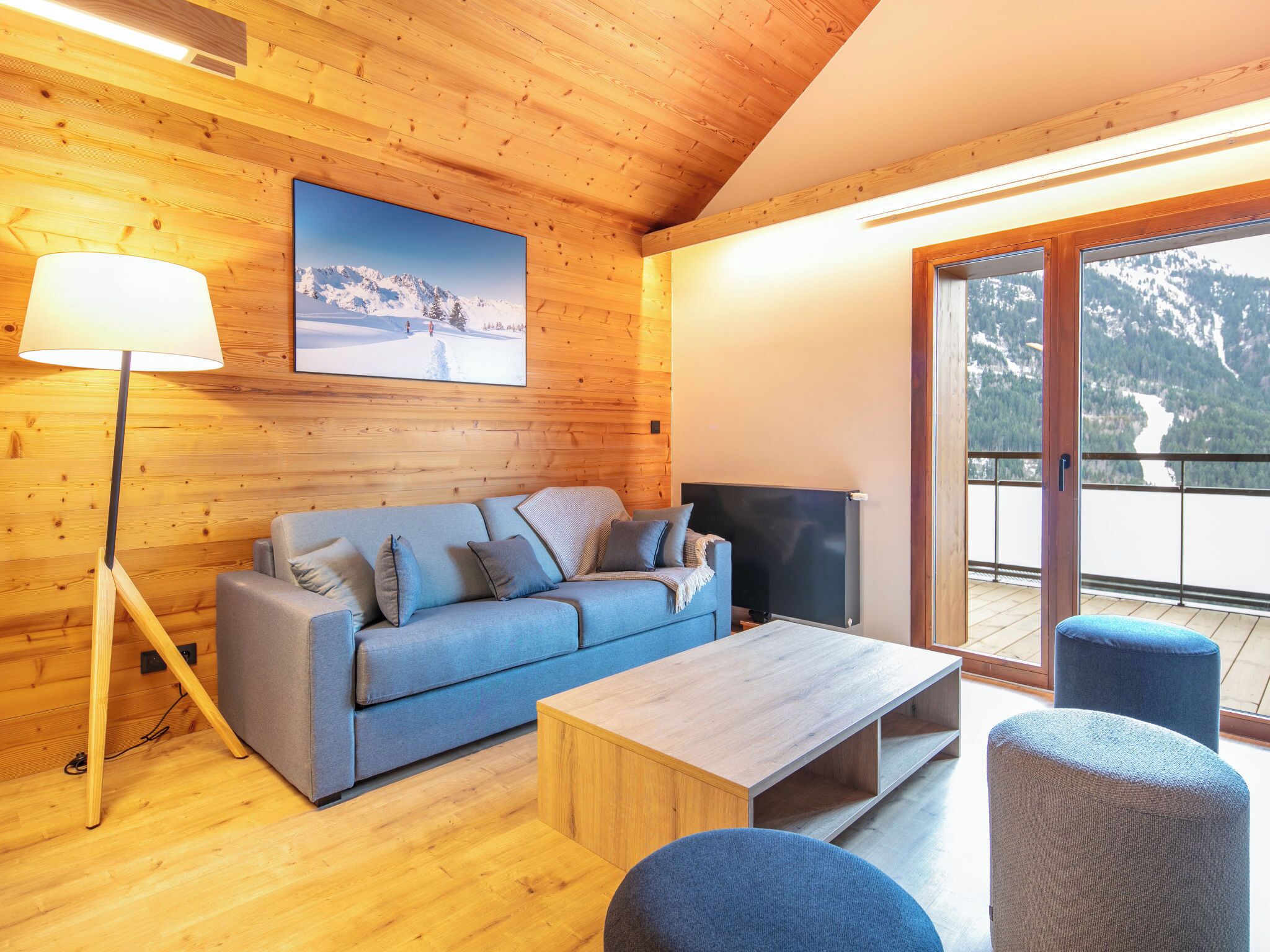 A wooden interior with a sofa, TV, and a balcony with a mountain view.