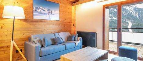 A wooden interior with a sofa, TV, and a balcony with a mountain view.