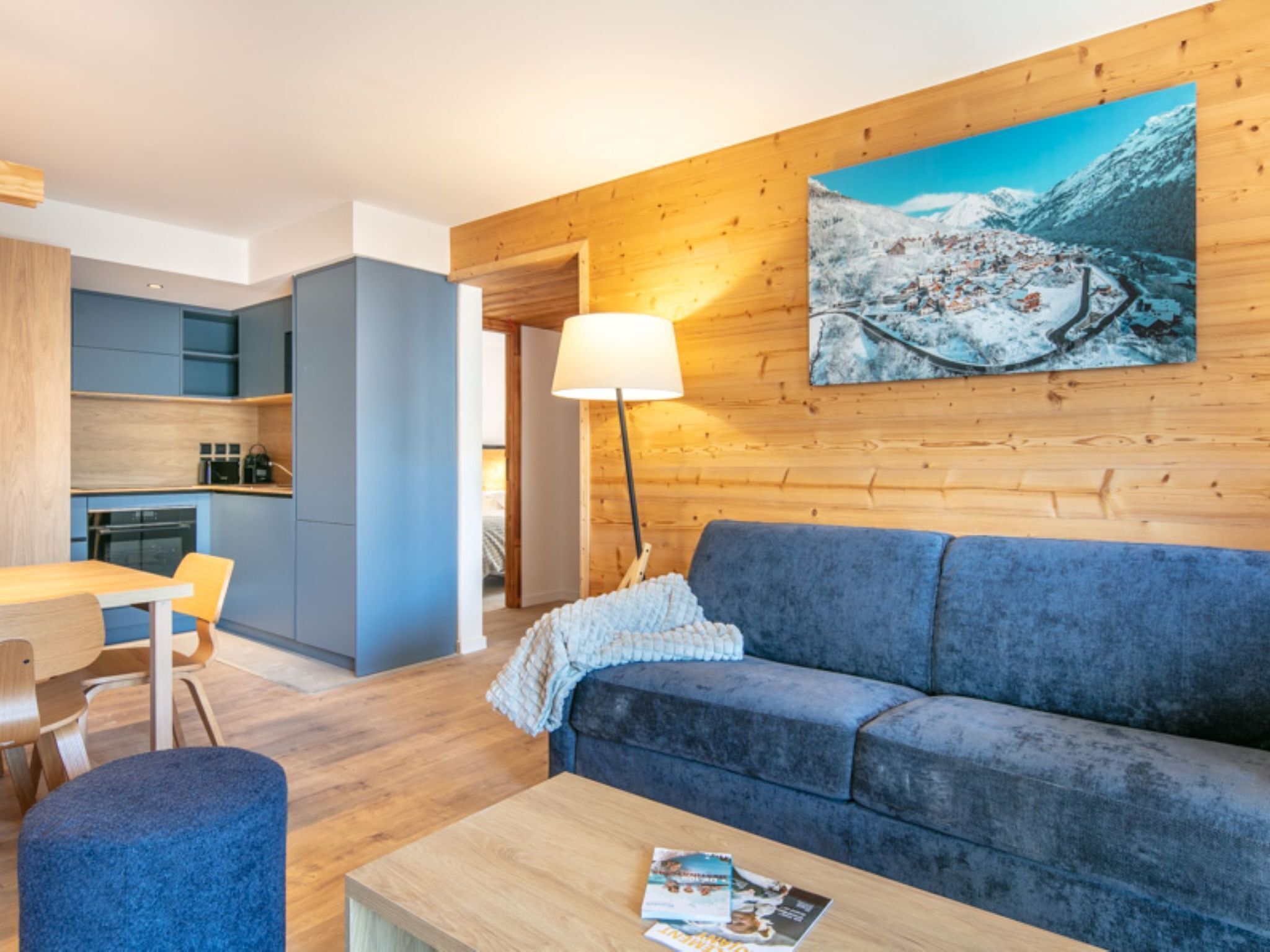 A modern living room with a sofa, a coffee table, and a painting of a snowy mountain landscape.