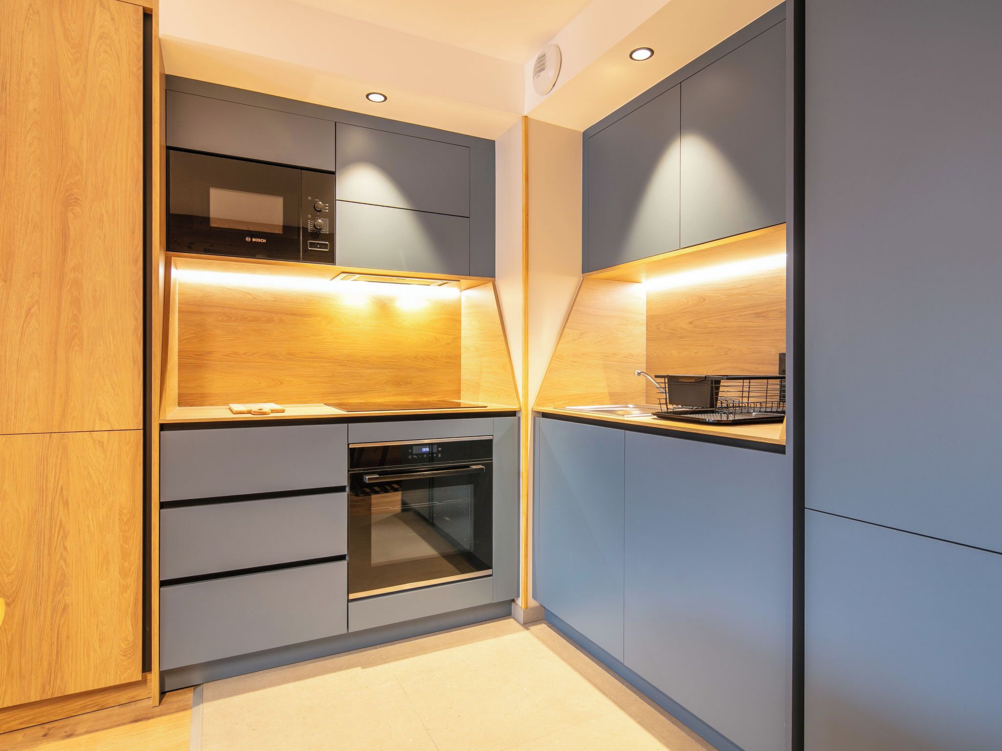 Cocina compacta con microondas Bosch, horno y encimera de madera.