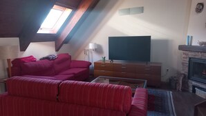 Un saló de tipus loft amb un sofà vermell, una televisió sobre un suport de fusta, una llar de foc i un finestral situat al sostre.