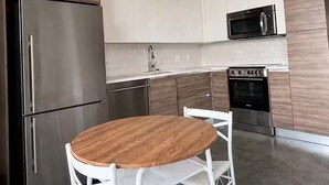 A modern kitchen with stainless steel appliances, white cabinetry, and a round wooden table with white chairs. - Downtown Dallas 2BR-2 Bath Loft (Dallas)