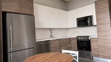 A modern kitchen with stainless steel appliances, white cabinetry, and a round wooden table with white chairs.