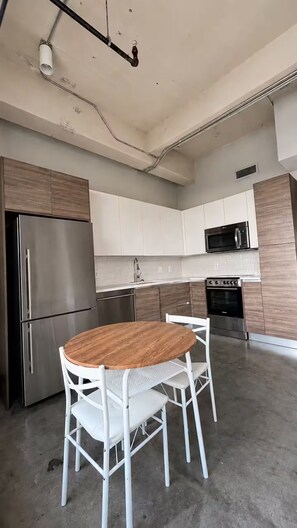 Eine moderne Küche mit Edelstahlgeräten, weißen Schränken und einem runden Holztisch mit weißen Stühlen.