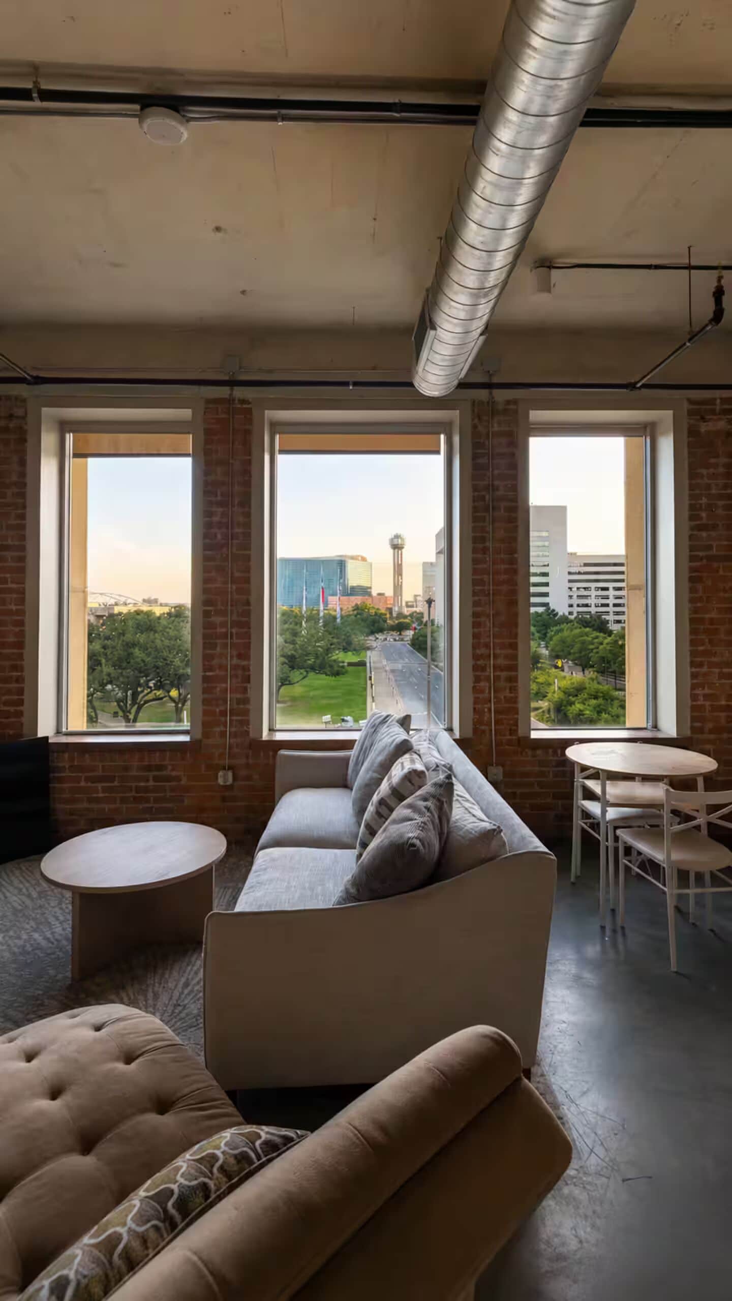 A modern living room with a sofa, a round table, and large windows offering a city view.