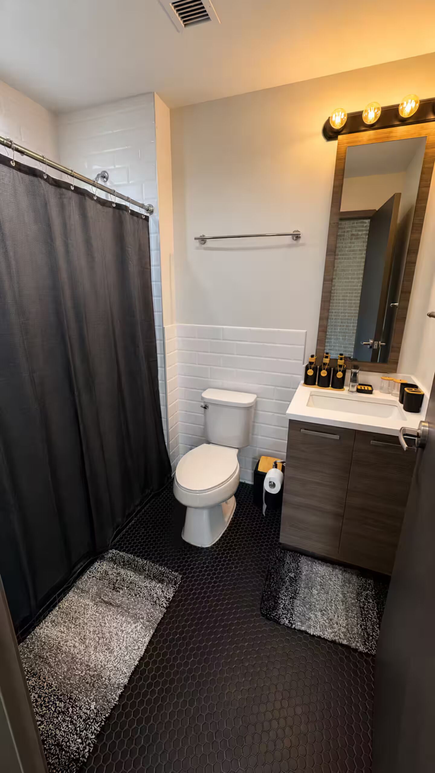 A bathroom with a shower, toilet, sink, and mirror.