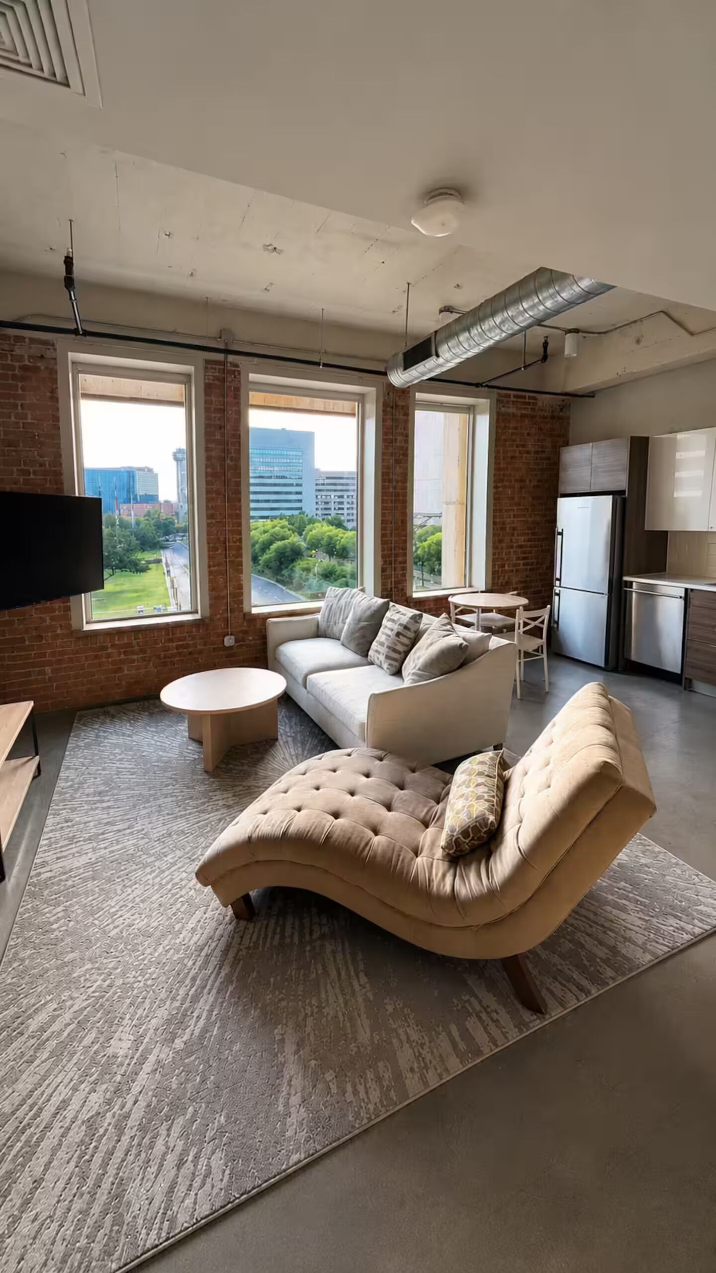 Un salon moderne avec un canapé, une table basse et une vue sur la ville grâce à de grandes fenêtres.