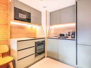 A modern kitchen with a Bosch microwave, oven, and dishwasher, wooden paneling, and a wooden chair. - Les Hauts de Vaujany by Interhome (Vaujany)