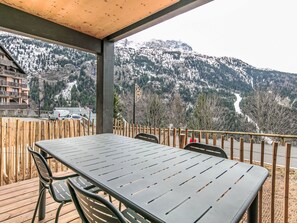 Ein überdachter Außenbereich mit Tisch und Stühlen, mit Blick auf eine Berglandschaft.