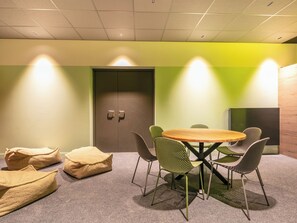 Een vergaderruimte met een ronde tafel, groene stoelen, een deur en een muur met groene accenten.