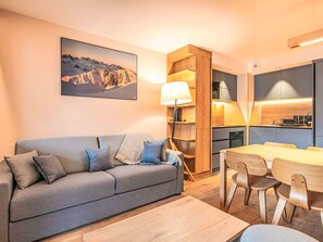 A modern living room with a sofa, a dining table, and a kitchen area. - Les Hauts de Vaujany by Interhome (Vaujany)