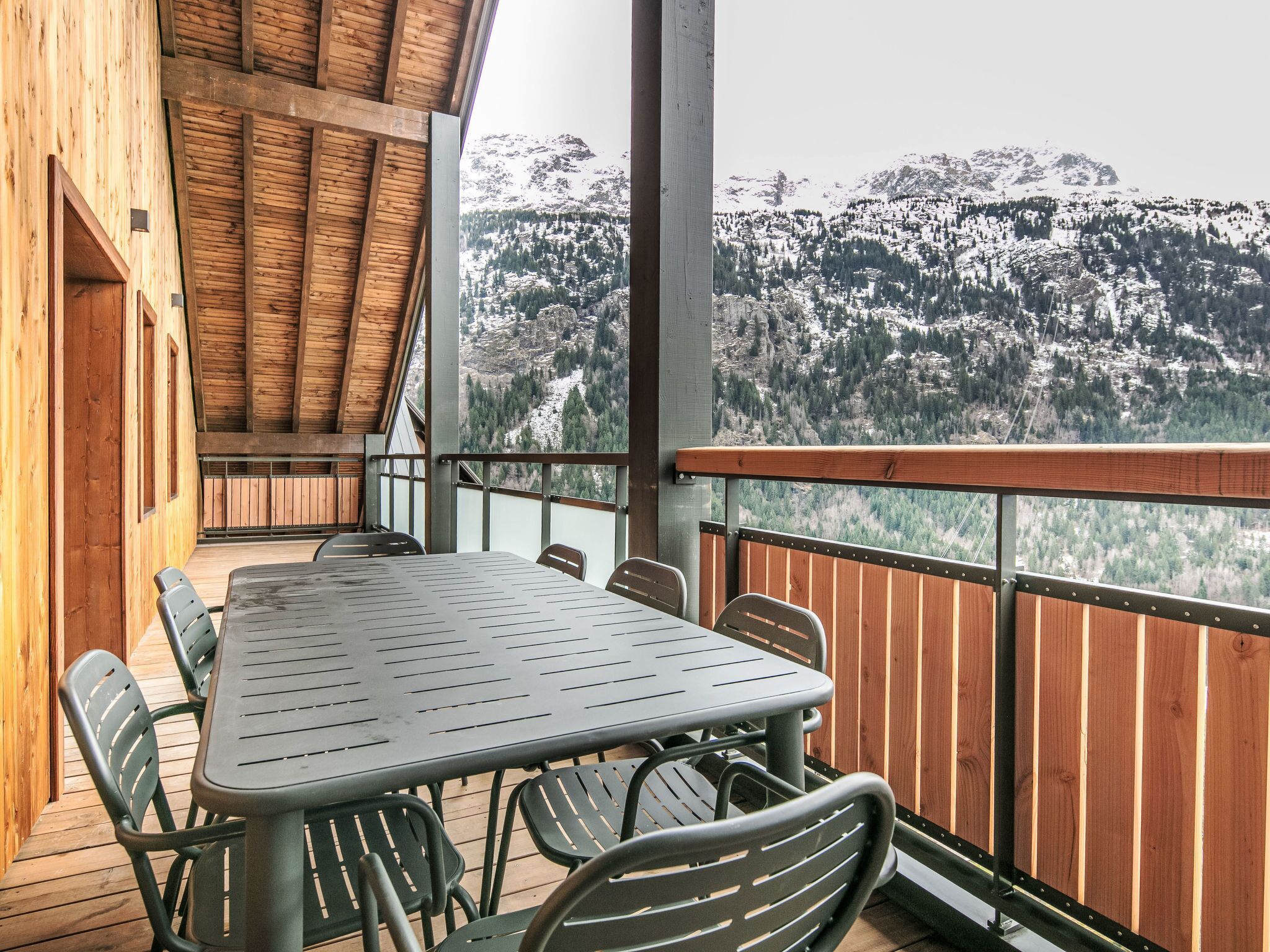 A wooden deck with a table and chairs, overlooking a snowy mountain landscape.