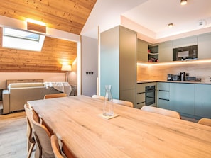 A modern kitchen with built-in appliances, a dining area with a wooden table and chairs, and a cozy seating area with a sofa and lamp. - Les Hauts de Vaujany by Interhome (Vaujany)
