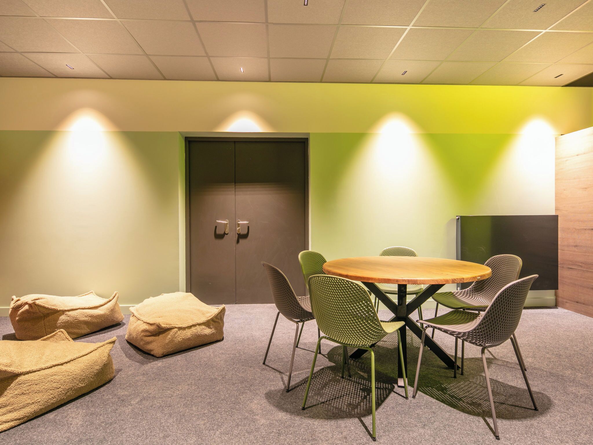 A conference room with a round table, green chairs, a door, and a wall with a green accent.