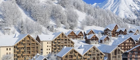A snow-covered lodge with multiple wooden buildings, a mountain backdrop, and a clear sky.