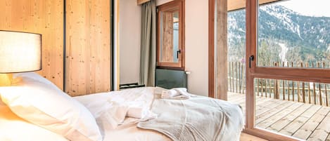 Un dormitorio con cama, paredes de madera, una ventana y un balcón con vistas a montañas.