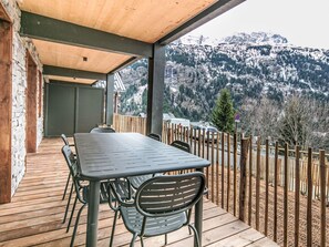 Een terras van hout buiten, met een tafel en stoelen, met uitzicht op een bergachtig landschap.