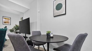 Una sala conferenze con un tavolo rotondo, quattro sedie grigie, un televisore nero e un quadro astratto incorniciato appeso al muro.