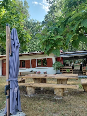 A wooden deck with picnic tables, a covered area with a hammock, and a building with red shutters. - La Halte de Dakota, a unique bed-and-breakfast nestled in the heart of nature. (Chamouillac)