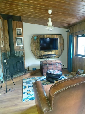 A living room with a wooden ceiling, a mounted television, a fireplace, a leather sofa, and a patterned rug. - La Halte de Dakota, a unique bed-and-breakfast nestled in the heart of nature. (Chamouillac)