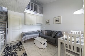 A room with a bed, a sofa, a dining table, a white chest of drawers, and a small white table with a lamp.
