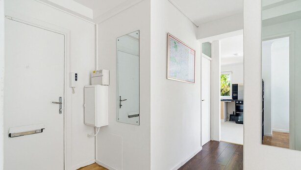 A hallway with white walls, a wooden floor, a door with a handle, a wall-mounted air conditioning unit, and a framed map. - New * Zone 1 - 2 bed slps 5 quiet modern 800mps Wifi a home from home! (London)