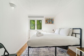 Een slaapkamer met een bed, een raam, een schilderij en een nachtkastje.