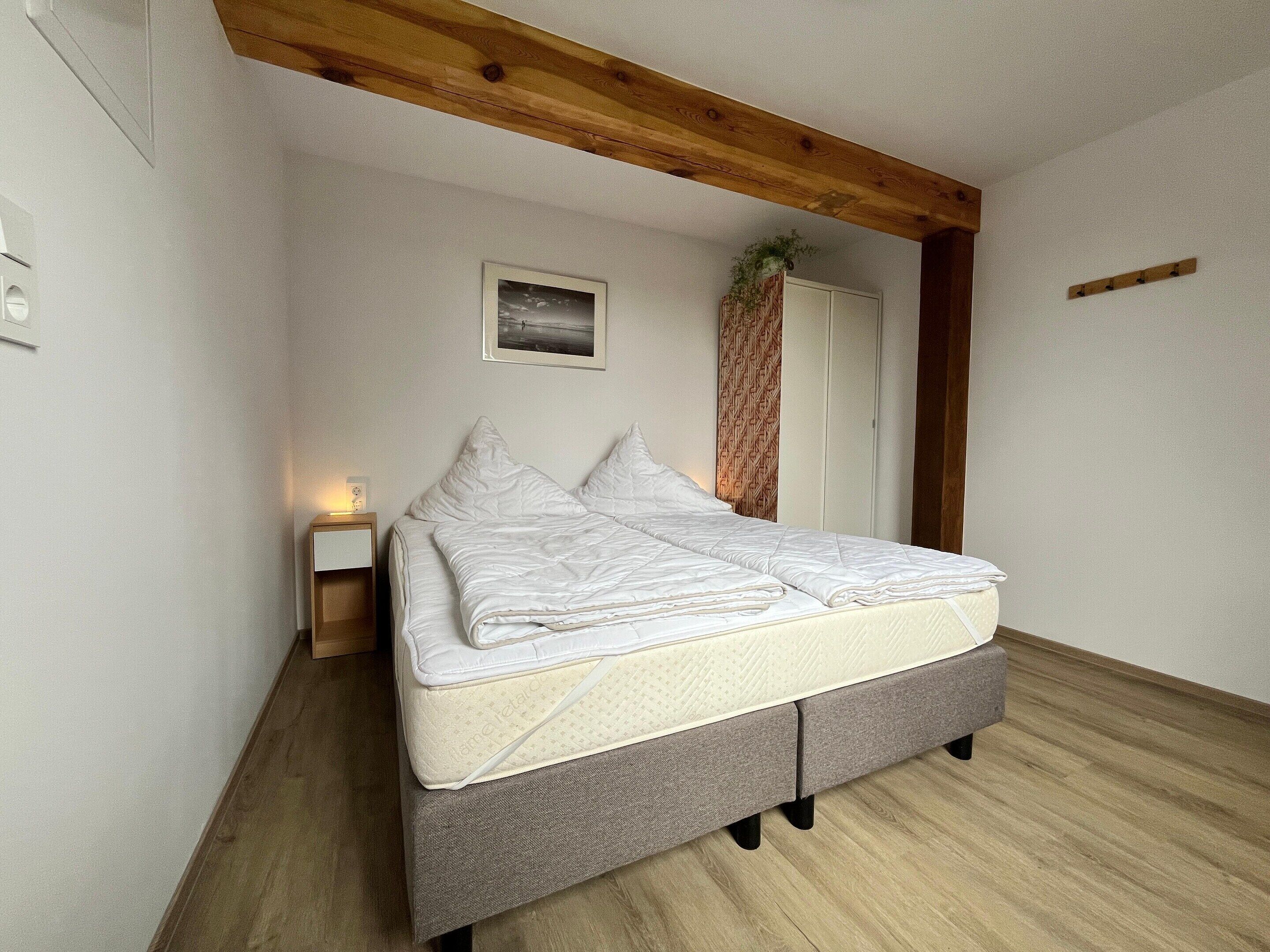 Une chambre à coucher comprenant un lit, une table de chevet, un tableau accroché au mur et une poutre en bois au plafond.