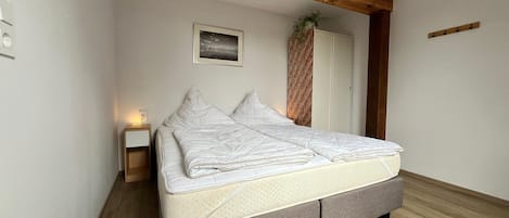 Une chambre à coucher comprenant un lit, une table de chevet, un tableau accroché au mur et une poutre en bois au plafond.