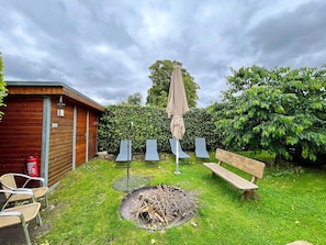 A backyard with a wooden cabin, a fire pit, outdoor seating, and a hedge. - Neues Appartement im Lepels Hof (Luetow)