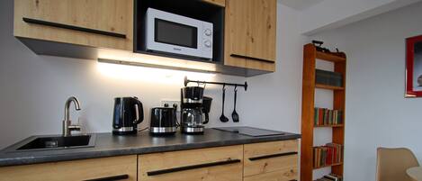 A kitchen with wooden cabinets, a microwave, a coffee maker, and a bookshelf.